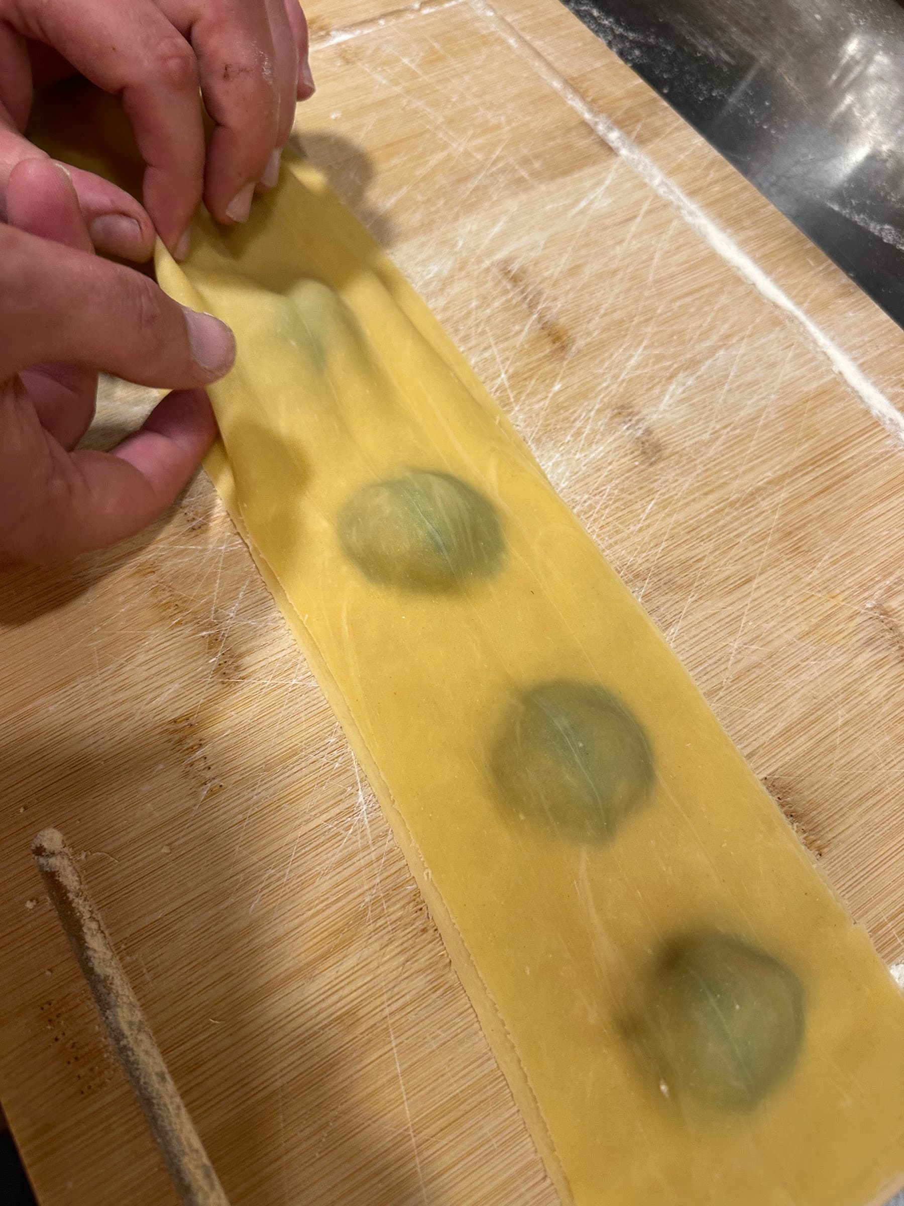 Manos que doblan la lámina de pasta sobre el relleno de los ravioli, en una tabla de madera